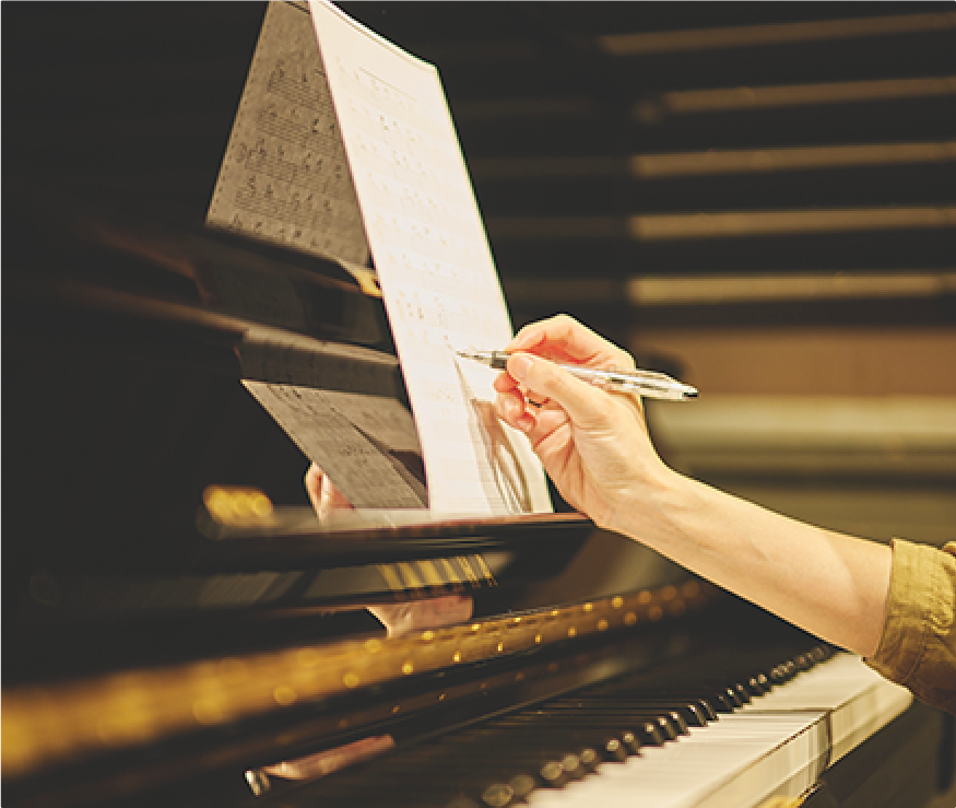 ピアノに向かって記譜をしている女性の手