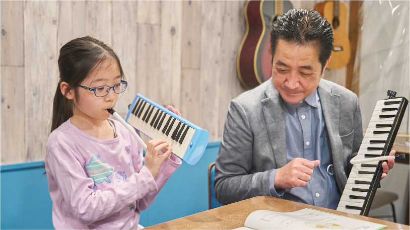 鍵盤ハーモニカを吹く小学生と講師